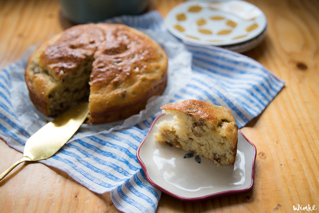 Een vers gebakken kwarkbrood op een houten tafel, gedeeltelijk gesneden met een gouden mes, naast een gestreepte doek en een schaaltje met boter.